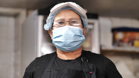 Slow-zoom-in-for-Portrait-of-Asian-female-chef-wearing-a-medical-face-mask,-glasses-and-black-uniform-in-the-kitchen