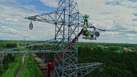 parallex drone shot of technicians on lifting crane working on high voltage electricity tower in their uniform