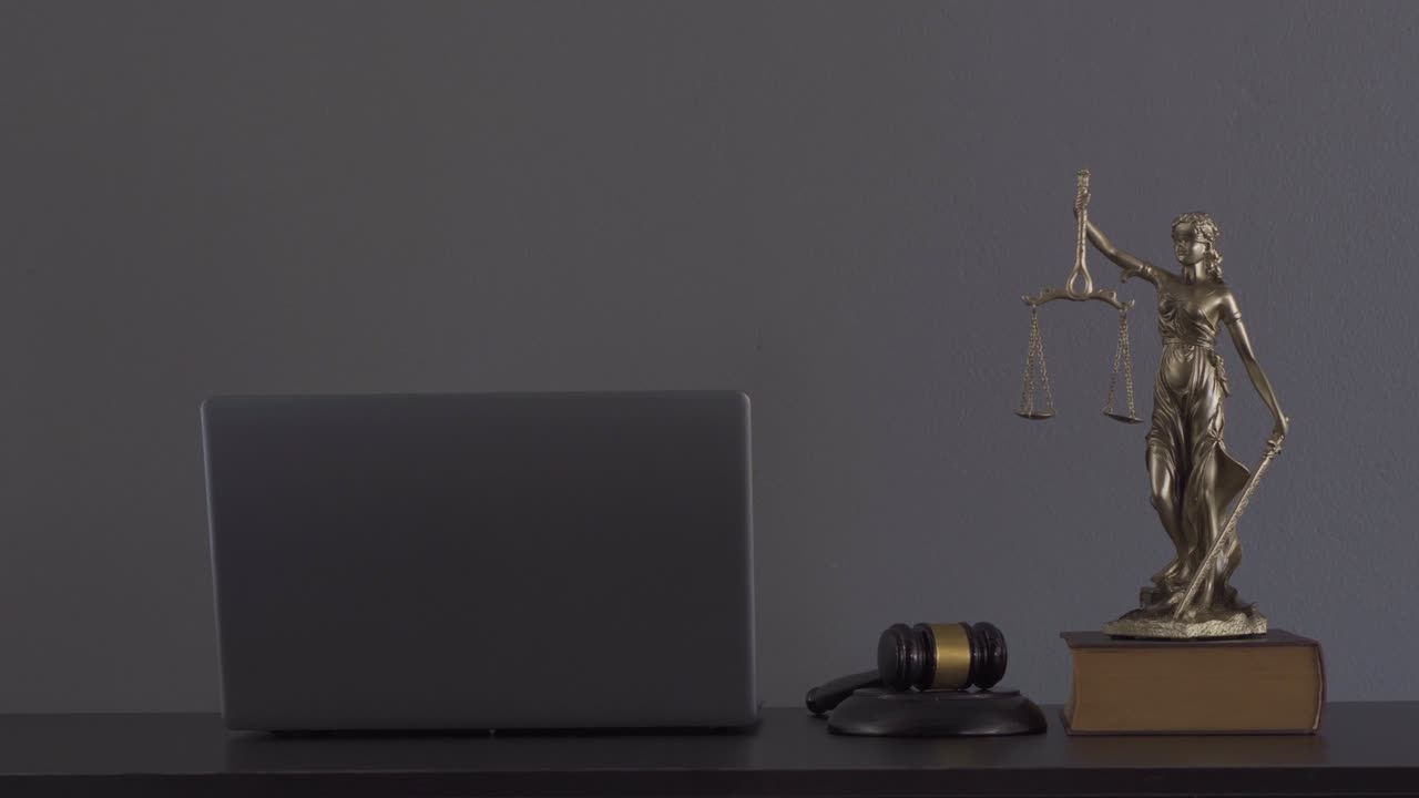 Laptop, martello del giudice, libri e bilancia. La dea della giustizia sul tavolo del concetto di consulenza legale.