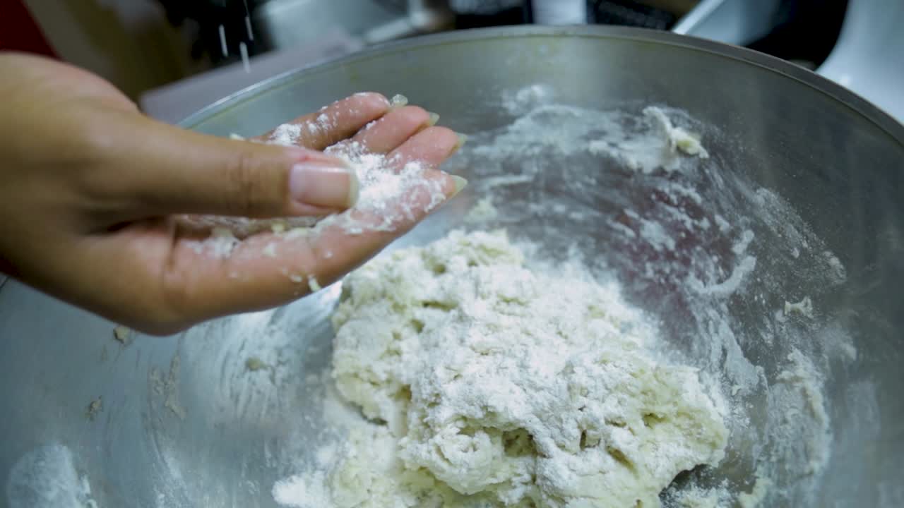close up view of African american woman's hands kneading pizza dough in a silver pan in slow motion