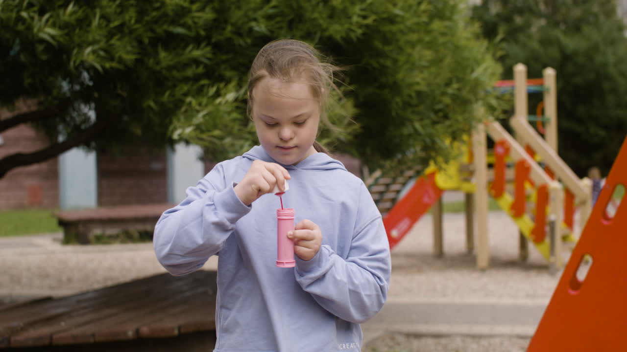 Little girl with down syndrome blowing soap bubbles in the park on a windy day