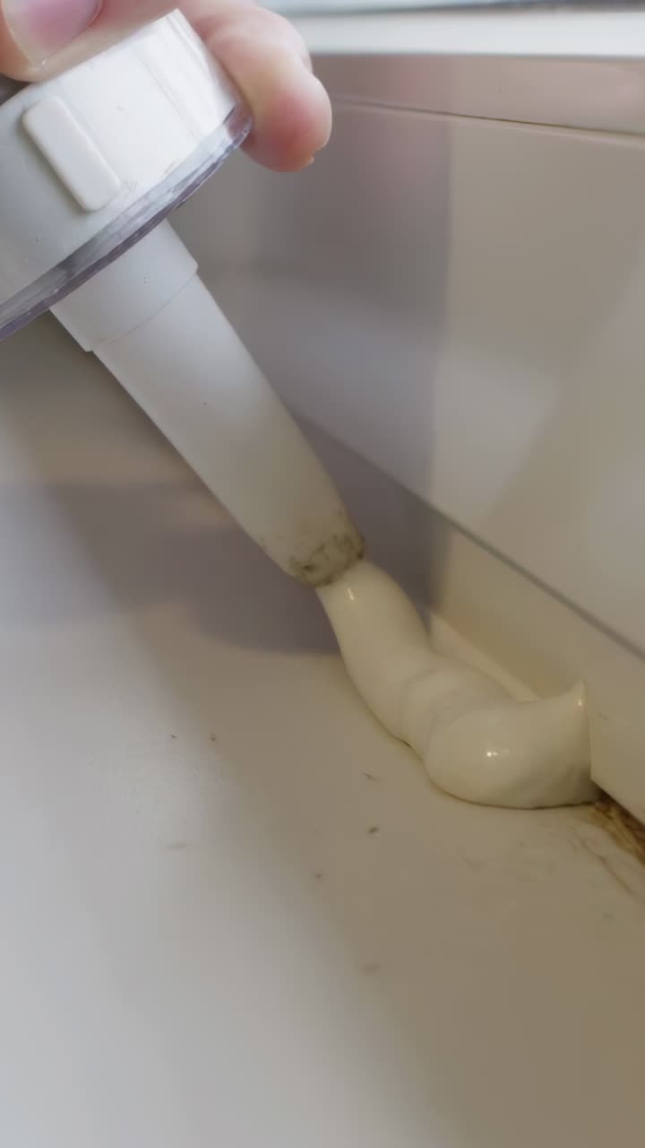 Vertical video: Pressing caulk tube, hand guiding nozzle laying bead along sill seam hiding residue