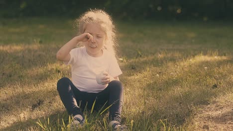 hungry girl enjoys eating delicious yogurt sitting on grass