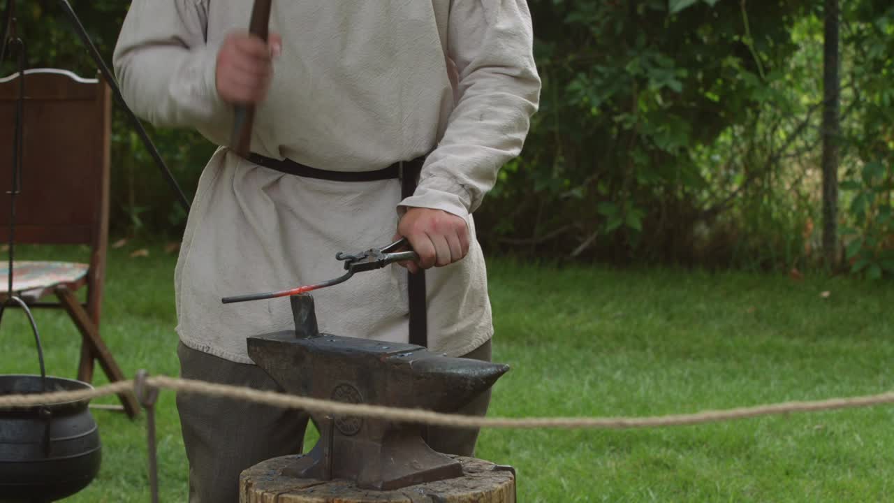 혁명 전쟁 재현가 대장장이가 모루에서 뜨거운 녹은 금속 조각을 망치질합니다.