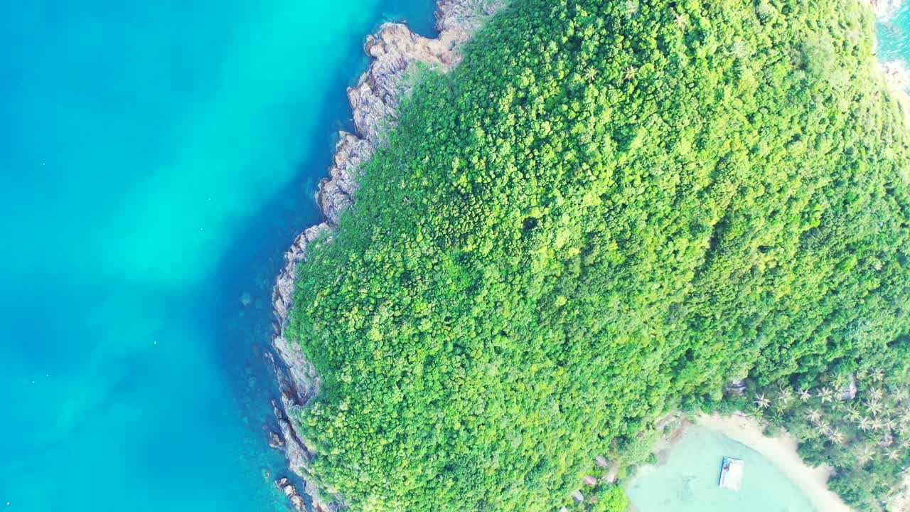 Remote tropical island with lush vegetation and rocky coastline surrounded by clear water of blue azure lagoon, Thailand