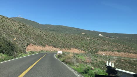 a view of a road and a big hill in the background from inside a car