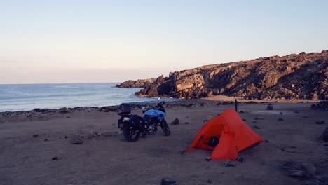 tienda de campaña naranja y motocicleta azul en la tranquila playa sombreada del océano en chile