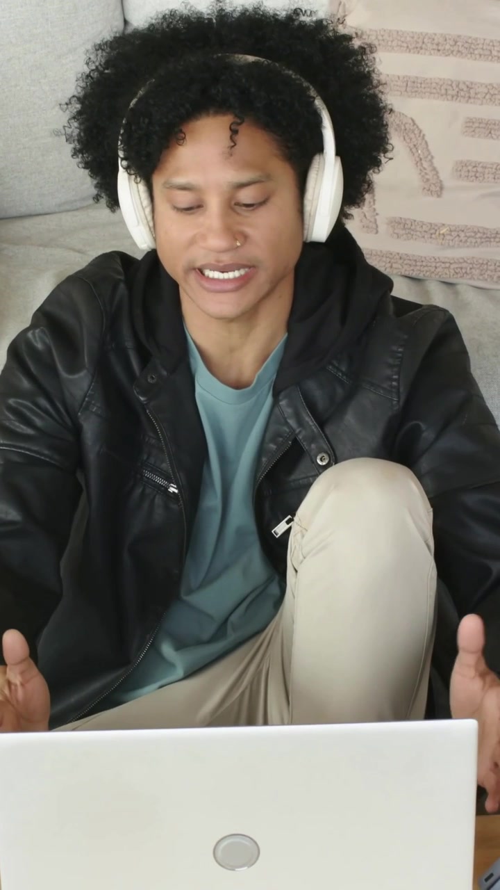 Vertical video: Putting glasses aside man wearing white headset speaking to laptop on couch on call