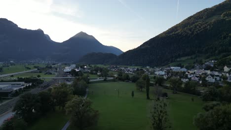 an aerial view over streets and residential areas surrounded by greenery and majestic mountains on a sunny day in switzerland