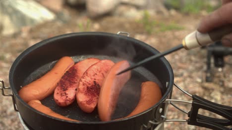 frankfurter sausages are flipped in frying pan on hot outdoor stove