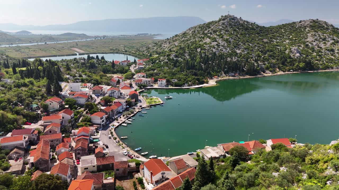 Aerial drone view over Rogotin, a peaceful village in Croatia’s Neretva Valley, with red rooftops, green hills and calm sunny landscape near Dubrovnik