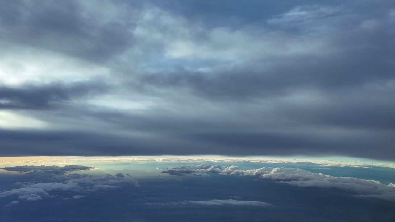 Pilot view from the cockpit of a jet airplane while flying under and endless layer of stratus clouds at sunset with a golden color horizon.