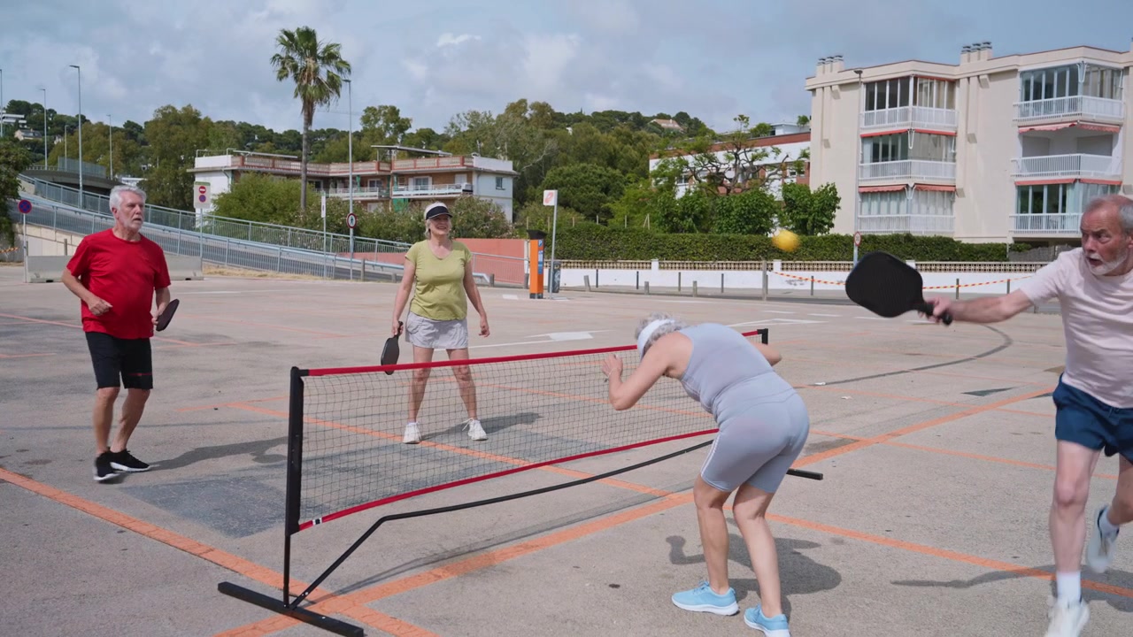 Cuatro adultos mayores jugando pickleball en una cancha al aire libre.