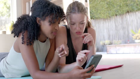 Mujeres-Felices-Y-Diversas-Tumbadas-En-Esteras-De-Yoga-Y-Usando-Teléfonos-Inteligentes,-Cámara-Lenta