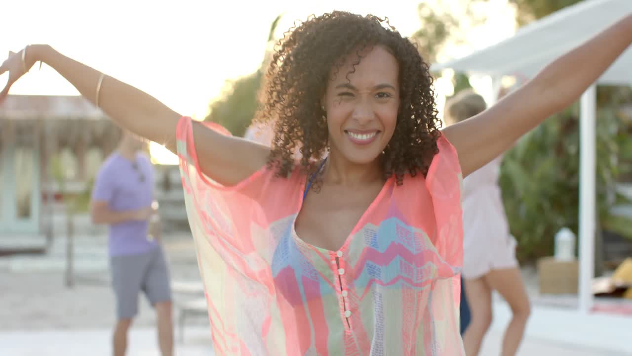 retrato de una mujer biracial feliz bailando con amigos en la playa.