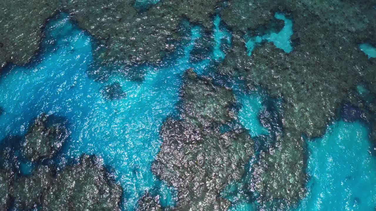 un dron captura una toma aérea de una laguna azul, mostrando las aguas cristalinas que revelan el impresionante paisaje submarino de rocas y vida marina debajo