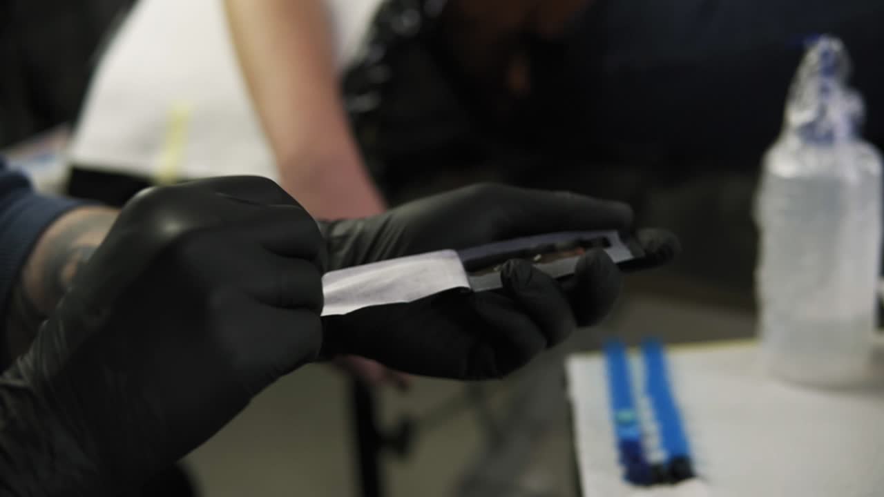 Tattoo master's hands in black gloves opens a new needle for a special pen for applying tatoo's ink. Microblading machine. Powder spraying, tattooing. Close up