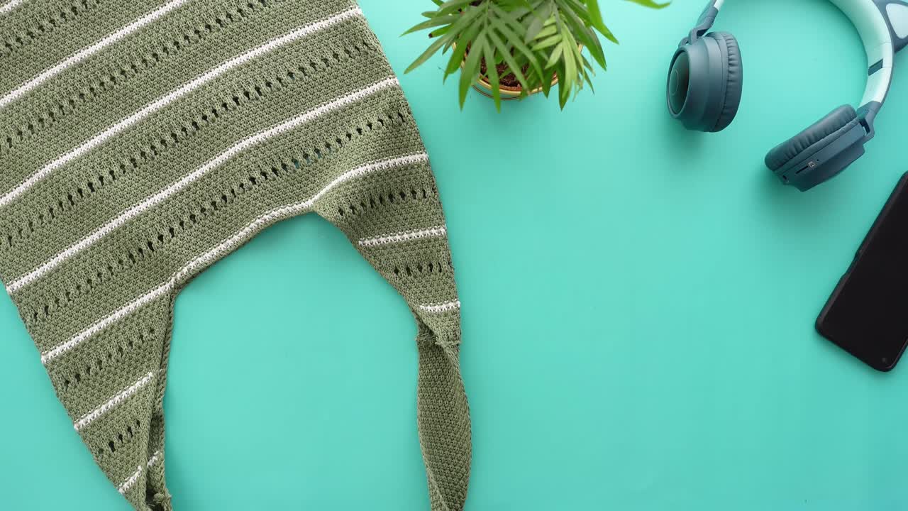 Flat lay of a knitted bag, plant, headphones, phone, and calculator