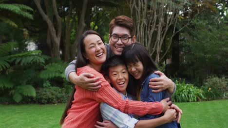 Smiling-asian-parents-hugging-happy-son-and-daughter-in-garden