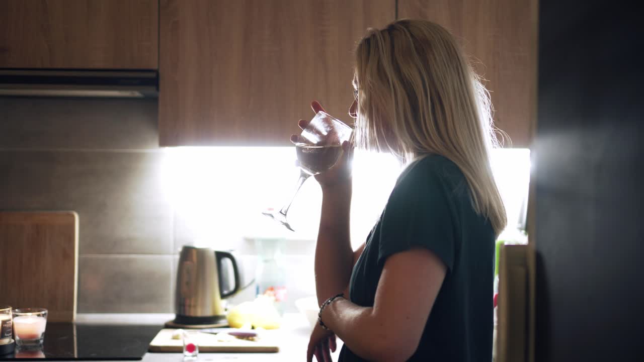 Girl drinking glass of white wine and singing in kitchen, house party