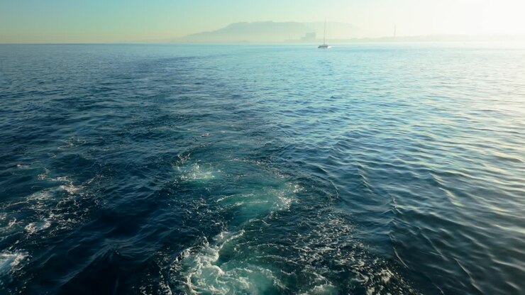 Vista di una barca a vela in lontananza sul calmo Mar Mediterraneo vicino a Malaga, con un orizzonte nebbioso e montagne sullo sfondo.