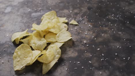 close up view of salt falling over potato chips with copy space on black surface