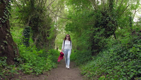 Young-woman-wearing-neutral-clothing-walking-along-a-woodland-path-on-a-sunny-day---model-released-4K-May-2021