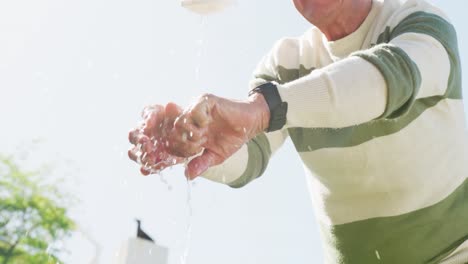 Happy-caucasian-senior-man-washing-hands-in-garden-on-sunny-day