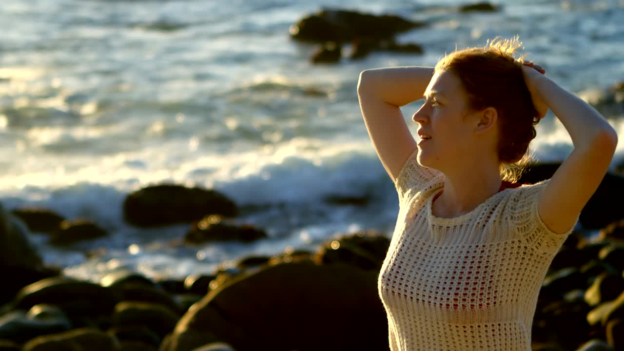 mujer de pie con las manos en el cabello en la playa 4k