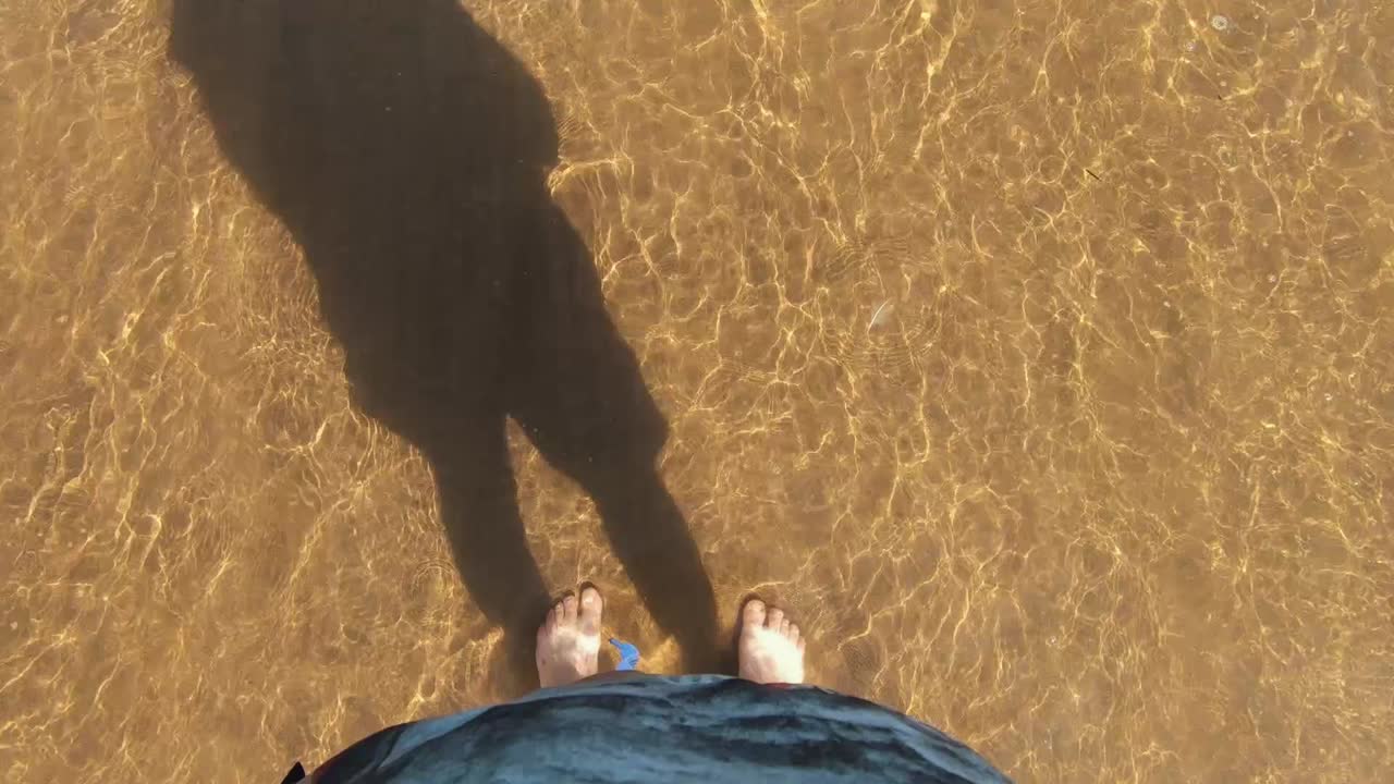 Piedi nel mare con le onde che si infrangono sulle gambe. Ripreso dall'alto.