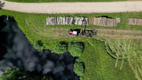 Tractor-trailer-loader-stacking-logs-along-a-countryside-road---straight-down-aerial-time-lapse