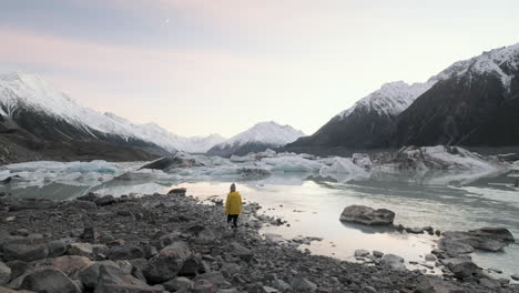 woman walking up to the edge of the glacial tasman lake on new zealand's south island