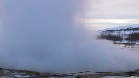 static mid shot of the great geysir in southwestern iceland exploding and creating a mist cloud with a midday sky back drop