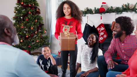 Nieta-Dando-Un-Regalo-Al-Abuelo-Mientras-Una-Familia-De-Varias-Generaciones-Celebra-La-Navidad-En-Casa