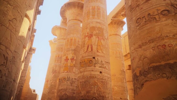 Large and detailed carved pillars in the Hypostile Hall, in Luxor Egypt. Images of gods and hieroglyphs carved into the stone. Slow pan.