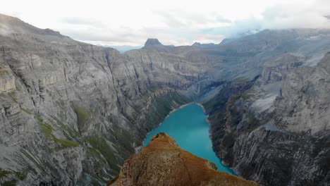 A-flyover-over-a-viewpoint-above-lake-Limmernsee-in-Glarus,-Switzerland,-with-hikers-enjoying-the-Swiss-Alps-view-with-cliffs-and-peaks-after-sunset-from-their-campspot