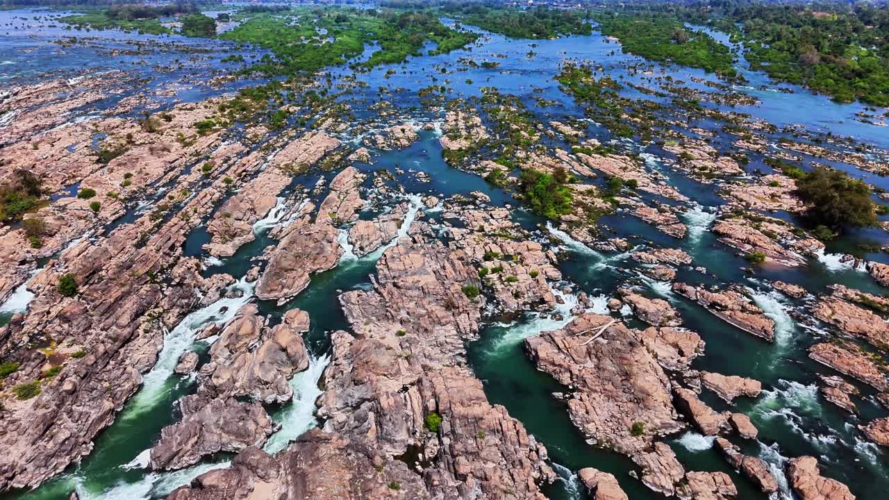 Wide top-down drone shot over Mekong River near Don Det, Laos, reveals interwoven rapids cutting through jagged rock beds and narrow channels across the fractured floodplain of the Si Phan Don region