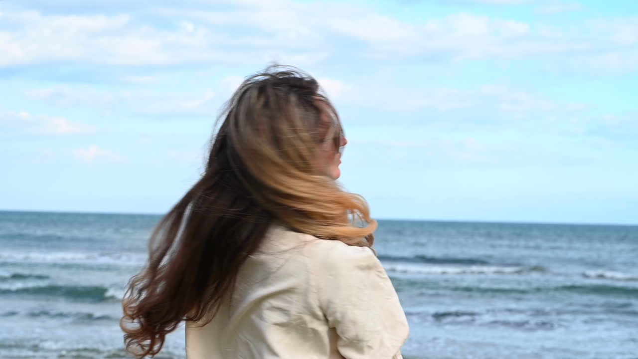 Stylish woman in sunglasses posing on Larnaca beach, Cyprus, with wind blowing through her long hair