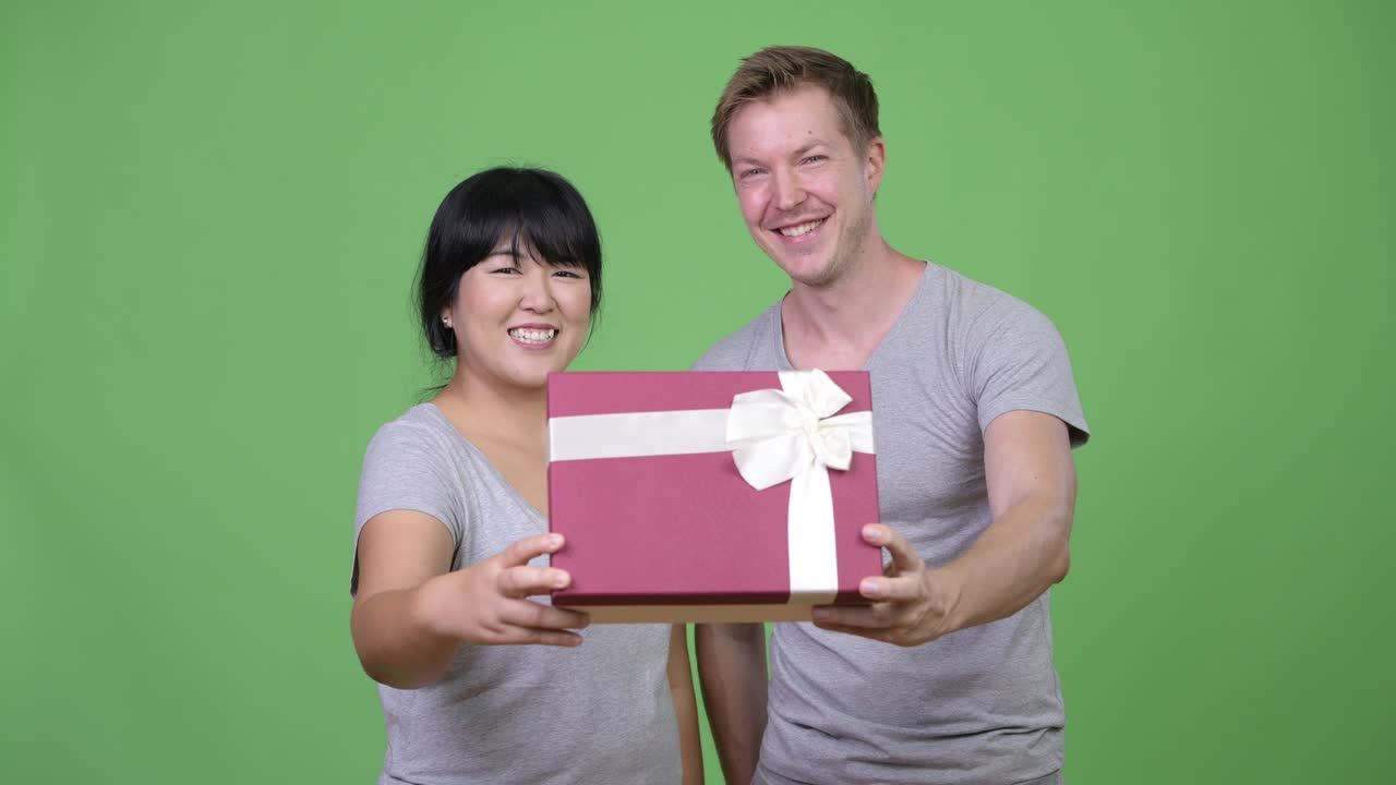 Young happy multi-ethnic couple giving gift box together