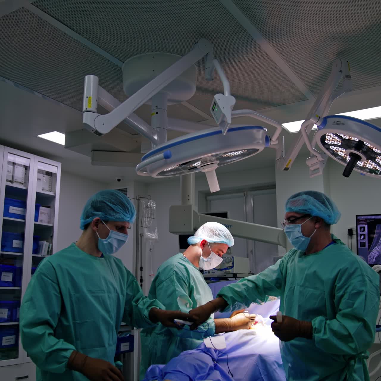 Doctor passes the used electric device to the assistant. Two doctors work under the round lamps in surgery room