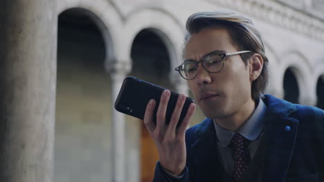 student recording voice message on cellphone. man using mobile phone outdoors