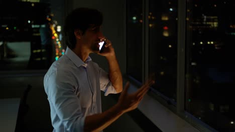 vista lateral de un joven ejecutivo caucásico hablando por teléfono móvil cerca de la ventana en una oficina moderna 4k