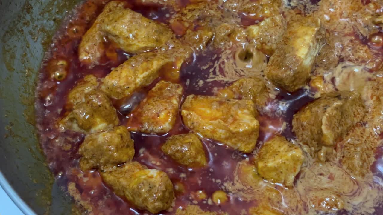 A close-up footage of boiling Thai curry with chunks of meat immersed in rich, spicy red sauce, bubbling intensely and releasing fragrant steam, showcasing vibrant flavors