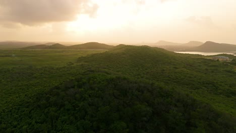 La-Luz-Dorada-Del-Amanecer-Se-Extiende-A-Través-De-Exuberantes-Colinas-Tropicales-De-La-Isla-Caribeña-De-Curacao,-Aérea