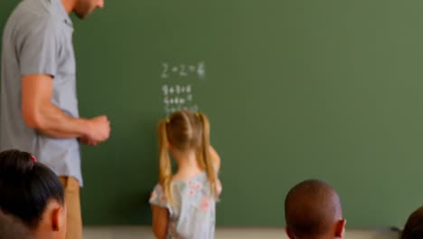Young-Caucasian-male-schoolteacher-and-schoolgirl-solving-math-problem-on-chalkboard-4k