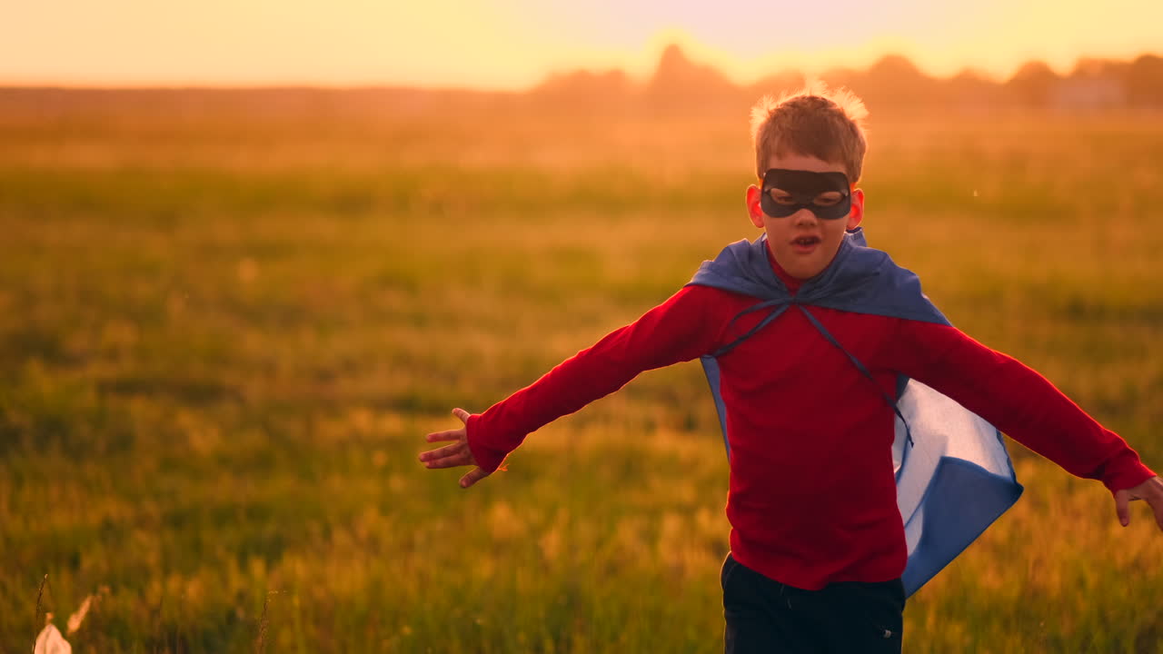 un niño con disfraz de superhéroe y máscara corriendo por el campo al atardecer soñando y fantaseando.