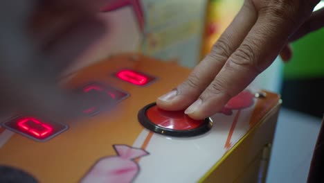 a close-up of a hand pushing a red button on an arcade game