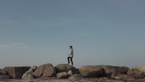 woman walking and jumping on series of big stones, extreme wide view