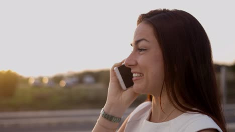 sonriente joven encantadora hablando en el teléfono inteligente en la calle.