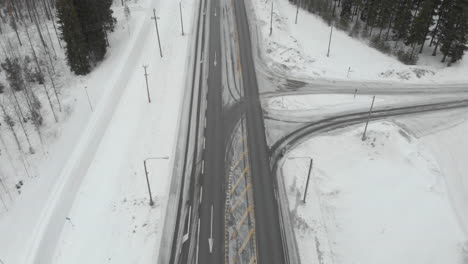 Aéreo,-Incline-Hacia-Abajo,-Tiro-De-Drone,-Sobre-El-Tráfico-En-La-Carretera-6,-Rodeado-De-árboles-Sin-Nieve,-Automóviles-Que-Giran-A-La-Derecha-Y-A-La-Izquierda-En-Las-Intersecciones,-En-Un-Día-Nublado-De-Invierno,-En-Kontionlahti,-Karelia-Del-Norte,-Finlandia